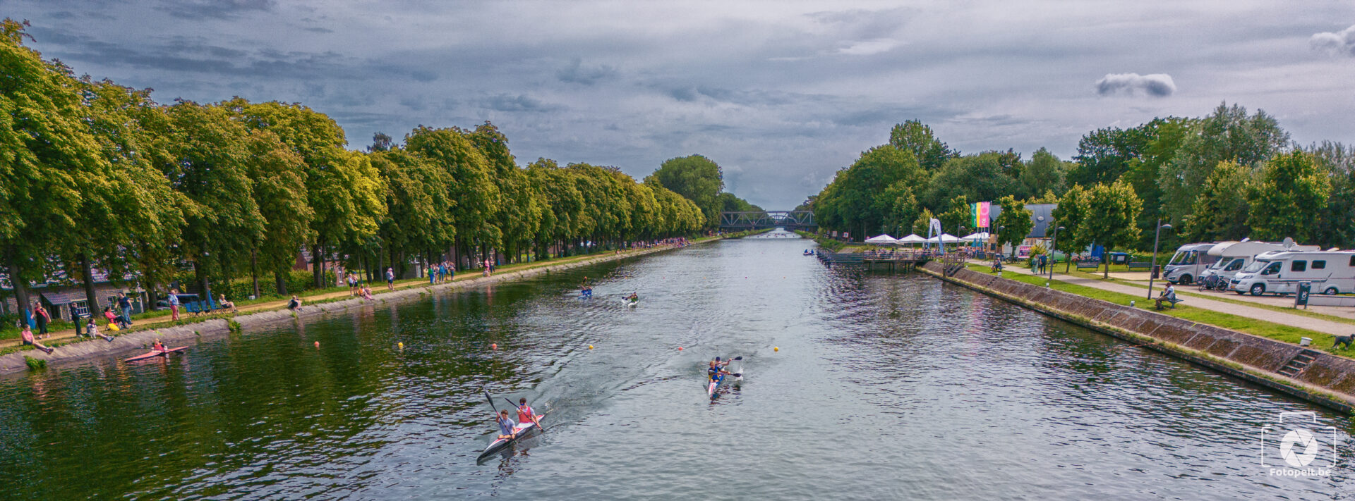 Kajakkers op het kanaal met publiek langs de oever.